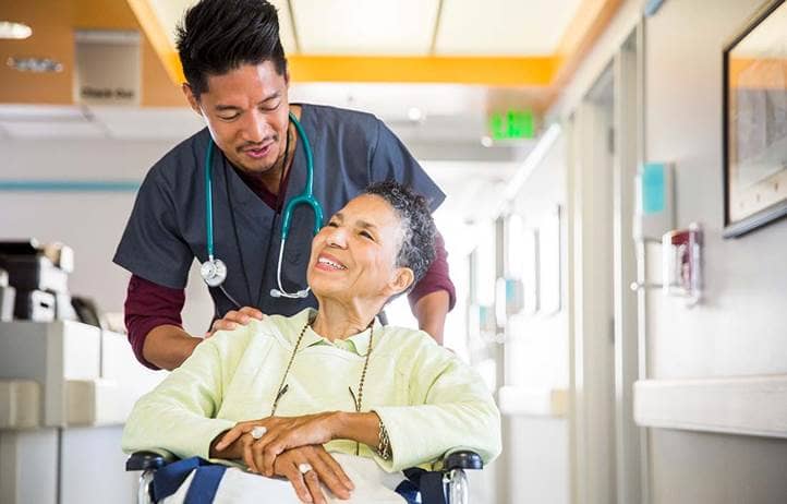 Nurse pushing senior woman in wheelchair in a long-term living facility.