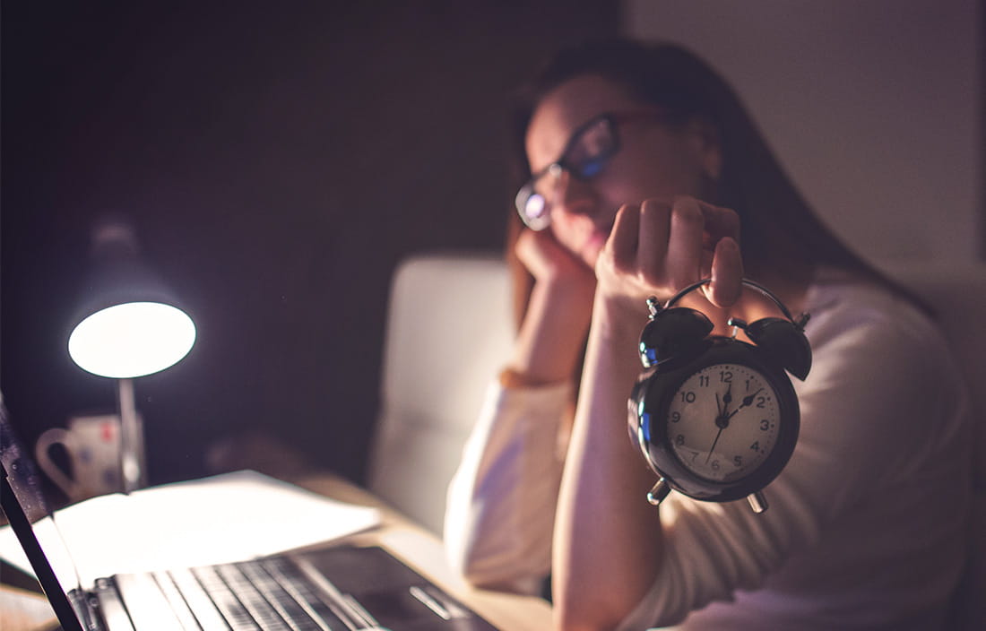 Image of woman holding an alarm clock while sitting at a desk