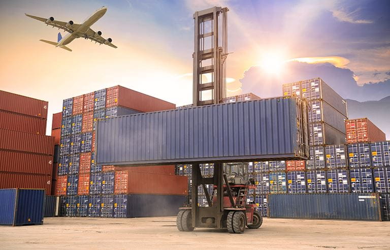 Shipping cannisters in large ship-yard with plane flying overhead.