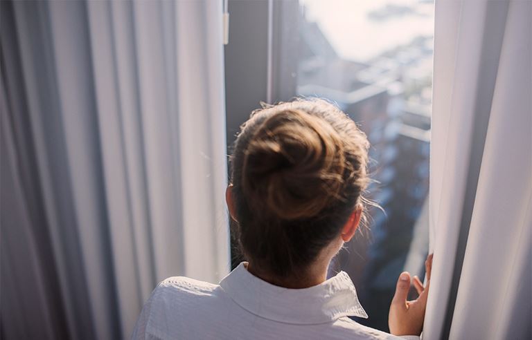 Image of woman looking out of window through drapes