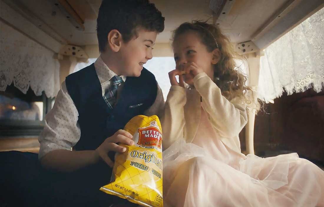 Two children under a kitchen table eating Better Made chips