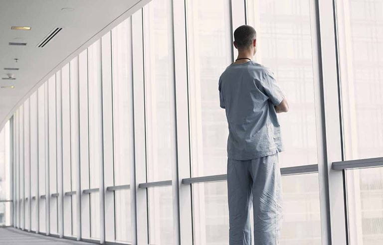 Doctor standing in a walkway looking out the window.