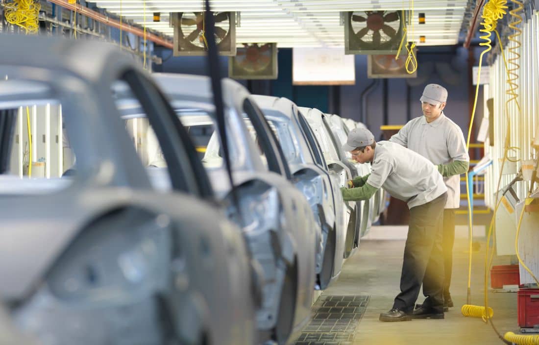 Two automotive factory workers assembling an automobile.
