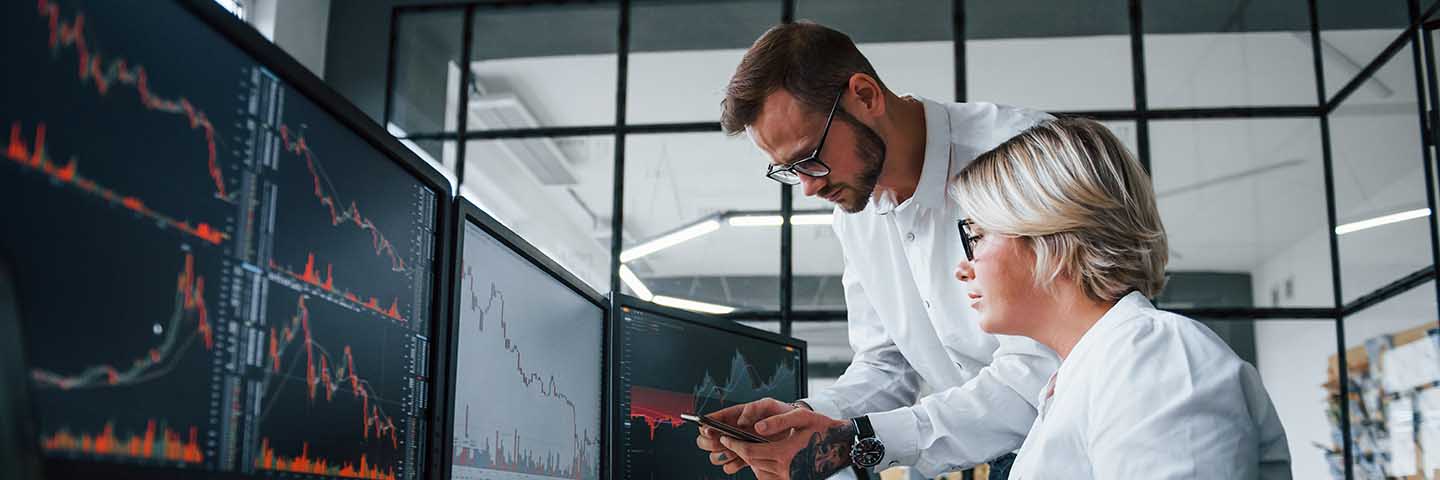 Two financial analysts looking at graphs on their computer screens.