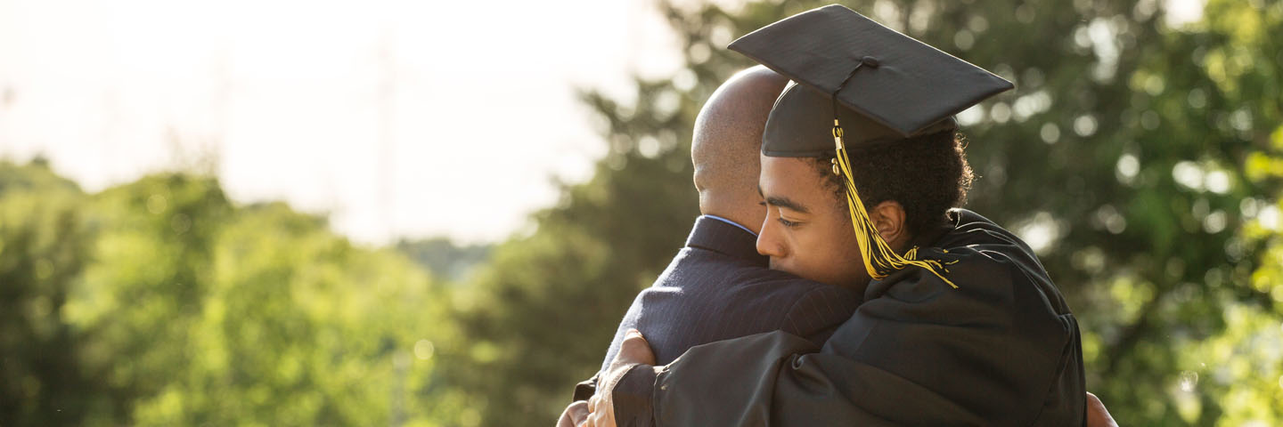 High school graduate in a cap and gown hugging their parent.