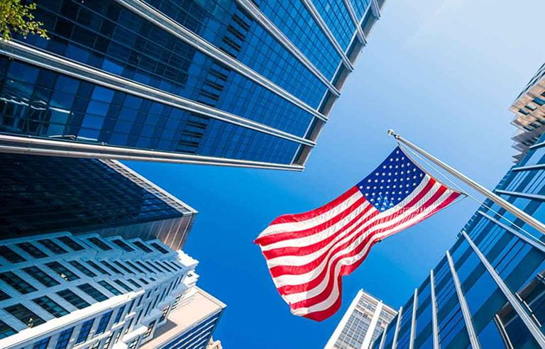 Looking up at American flag waving with buildings in the background.