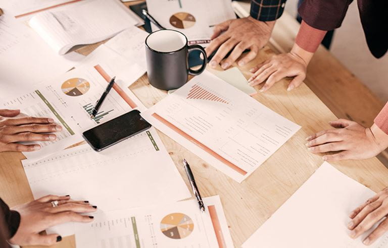 People's hands on a table with papers spread out.