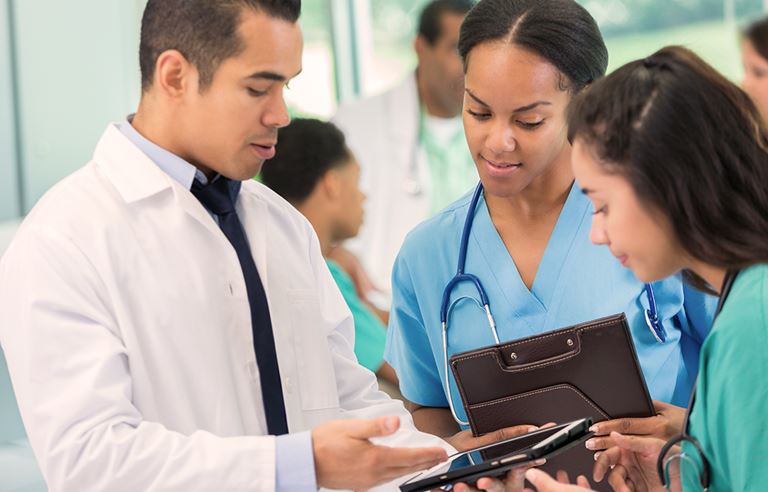 A doctor discussing a patients health chart on a tablet with two nurses.