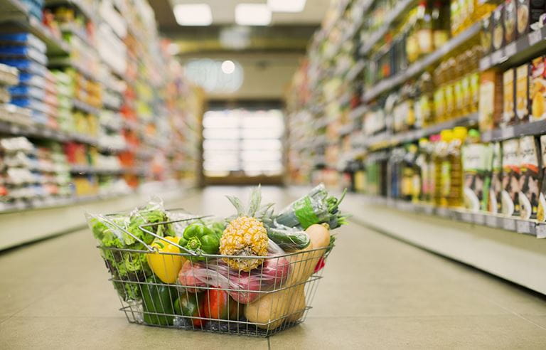 Basket of fruit and vegetables sitting in a grocery store aisle.