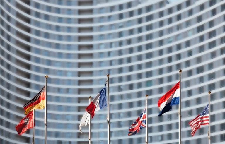 Numerous countries flags on flagpoles in front of a business building.