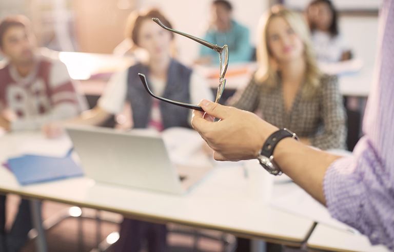 A teacher standing in front of a classroom of college students. 