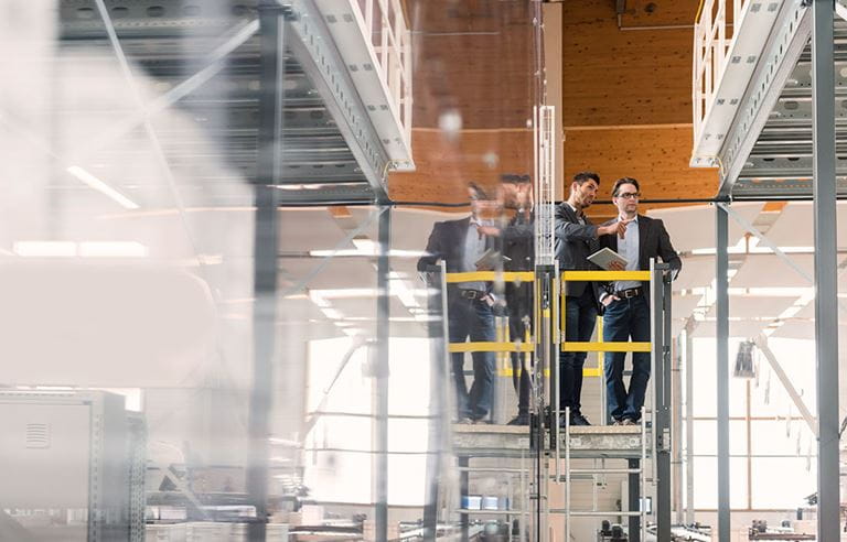 Two business colleagues on a scaffold in a warehouse examining shelving units. 