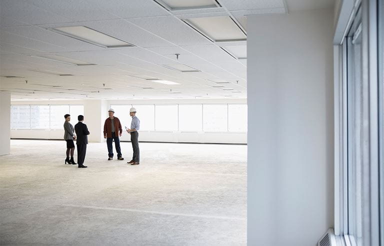 Dos profesionales de negocios discutiendo planos de oficinas con dos trabajadores de la construcción.