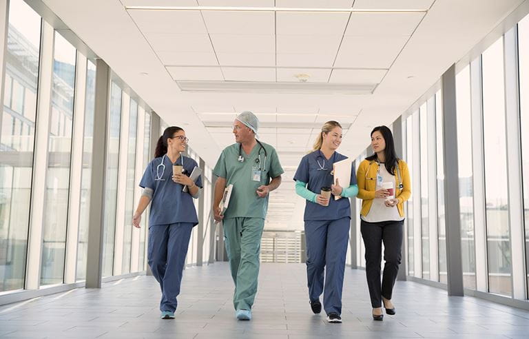 Four physicians and doctors walking down a glass hallway corridor.