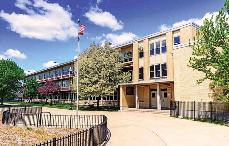 Three-story school building with an American flag in the front courtyard. 