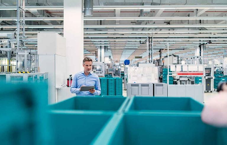 Factory worker inspecting work stations and factory lines with a tablet in his hand. 