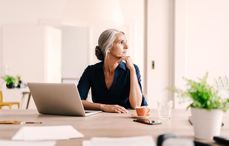 Middle-aged woman sitting at kitchen table with laptop computer. 