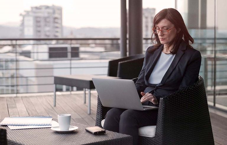 Woman sitting in an outdoor area for a building using her laptop computer.