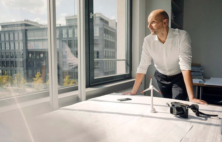 Business executive leaning on a table while looking out his office window.