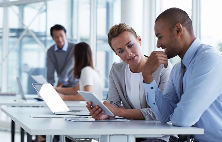 Business professionals reviewing information on a handheld tablet together.