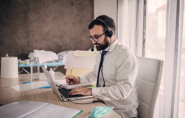 Man sitting at his desk, typing on is laptop and wearing a headset