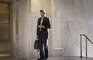 Businessman standing at the top of a staircase looking down and checking his cell phone.