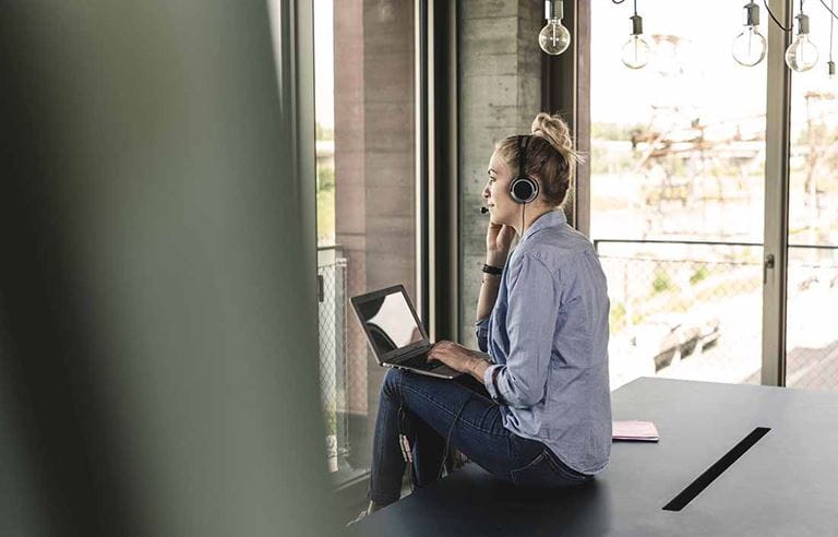 Woman sitting on a table on her laptop while talking on a headset