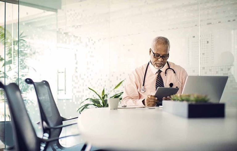 Healthcare worker sitting at a table with his laptop and tablet