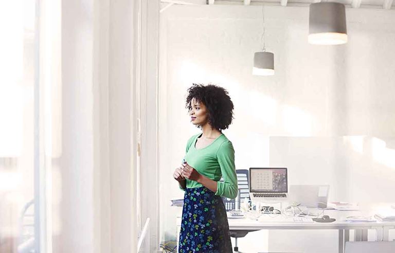 Woman standing in an all white office, looking out the window