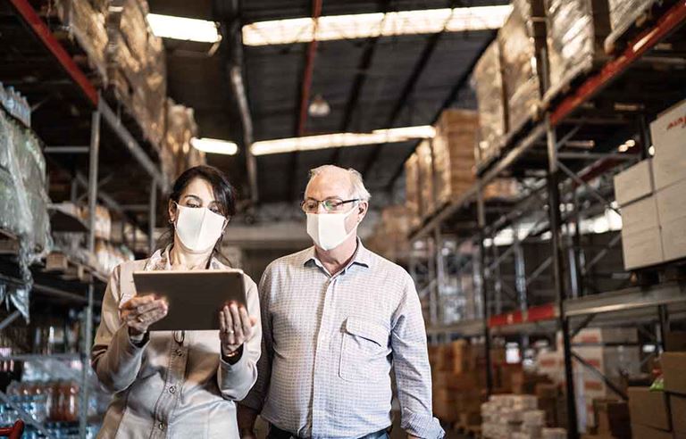 Two workers in a warehouse wearing protective facemasks.