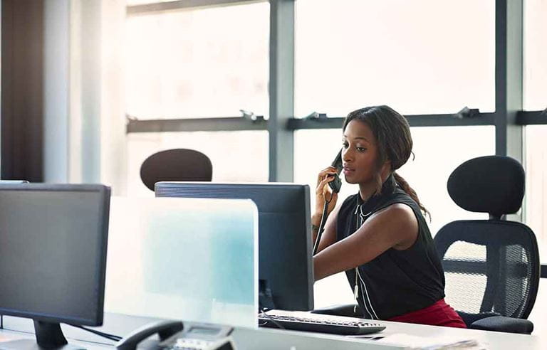 Businesswoman taking a phone call while looking at her computer monitor.