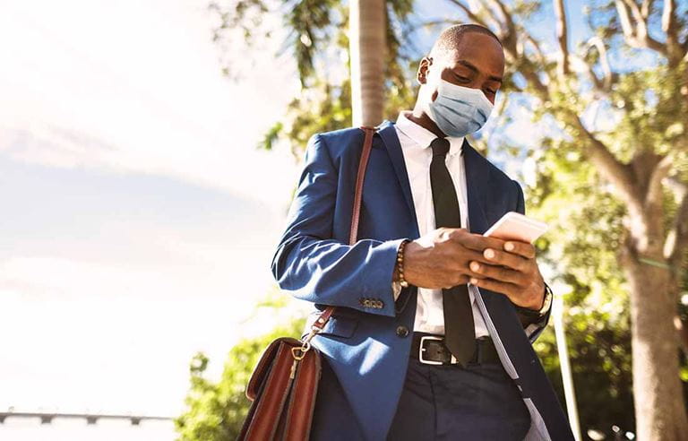 Businessman walking outside wearing a protective facemask for COVID-19.