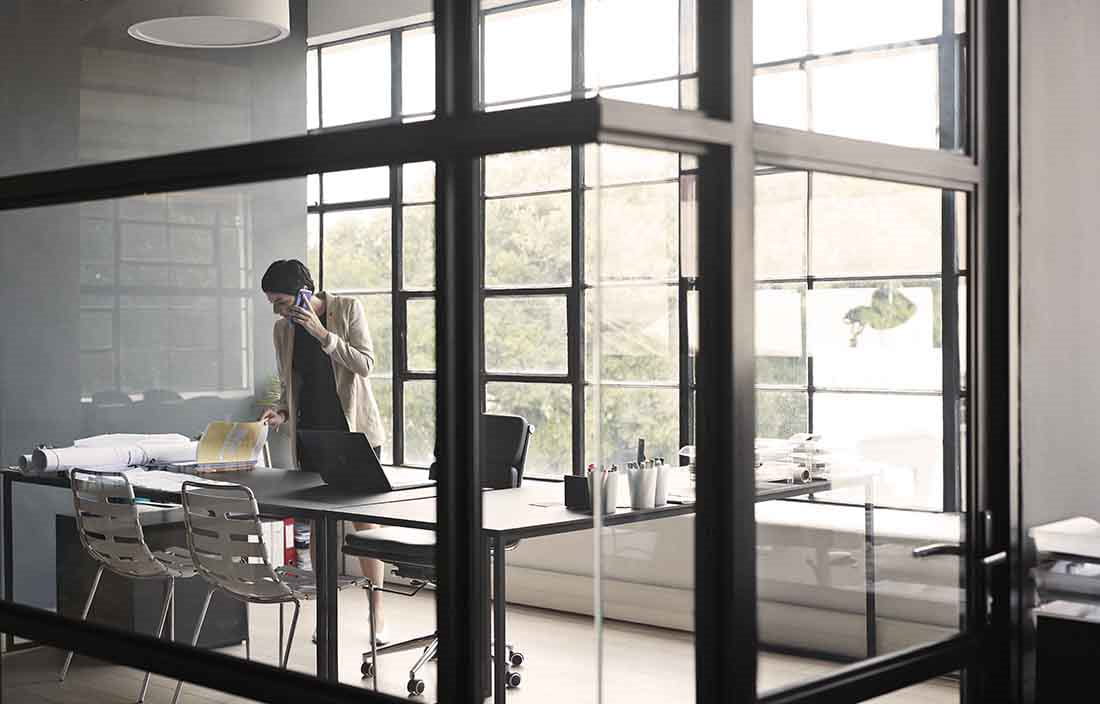 Businesswoman standing in a side conference room taking a phone call.