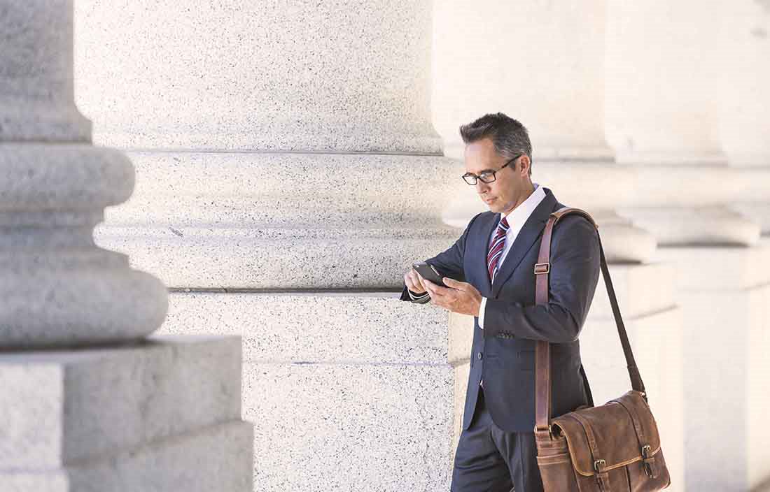 Businessman checking cell phone standing next to pillars of a government building.