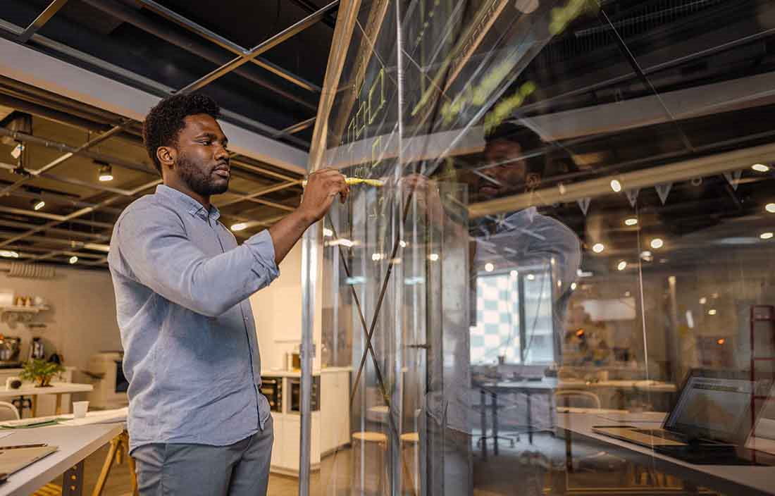 Businessperson using a marker on a glass writing board in the office.