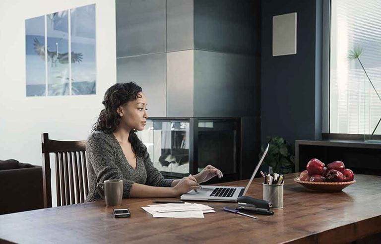 Businessperson working at home using a laptop computer at a kitchen table.