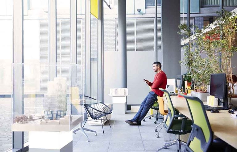 Business professional leaning against a desk while using their cell phone.