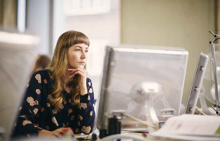 Businesswoman sitting at a desk looking at a computer monitor.