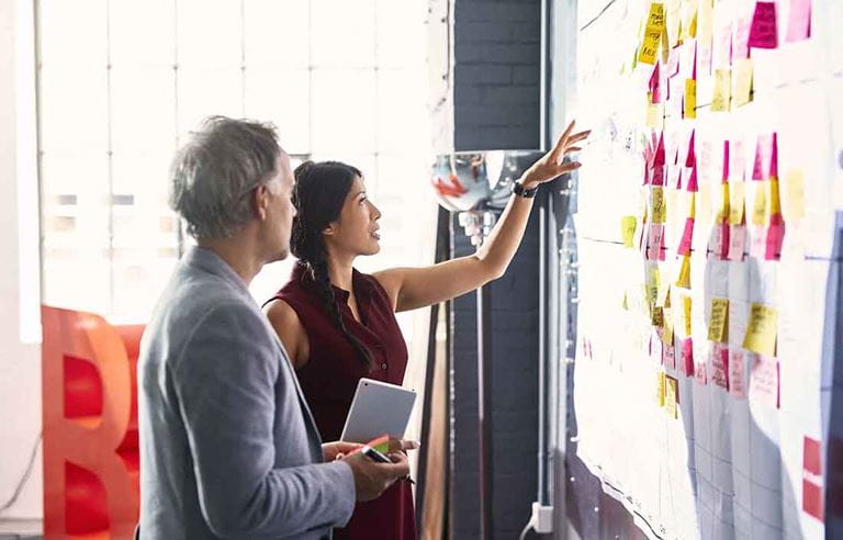 Businesswoman pointing at a board with post-it notes stuck to it.