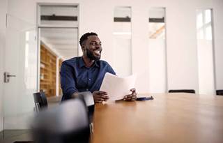 Business professional sitting at a conference room table holding a piece of paper and smiling.
