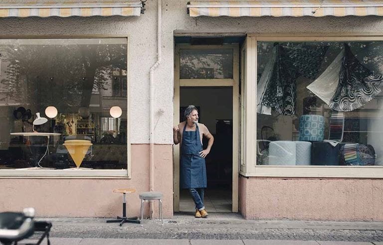 Shop owner standing outside their storefront on the sidewalk.