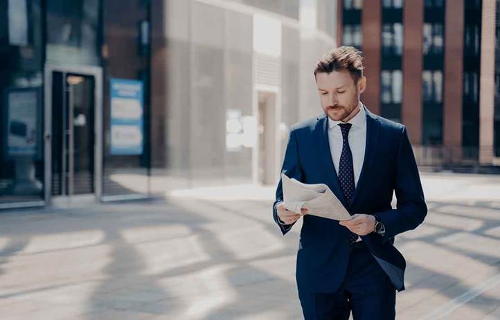 Business professional standing outside reading a newspaper.