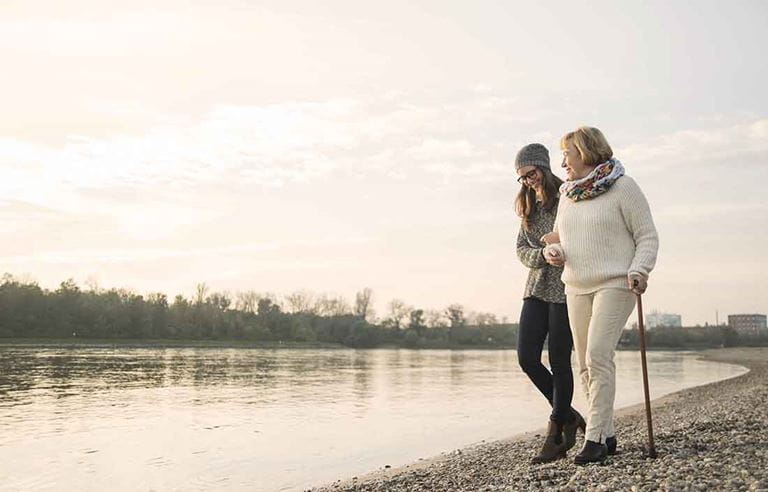 Senior care worker walking with an elderly senior citizen nearby a lake shore.