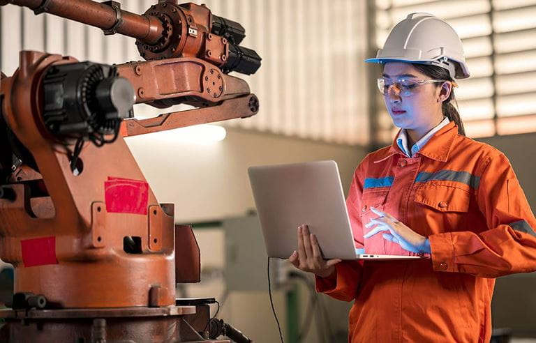 Manufacturing worker in a hardhat next to an automated robot arm.