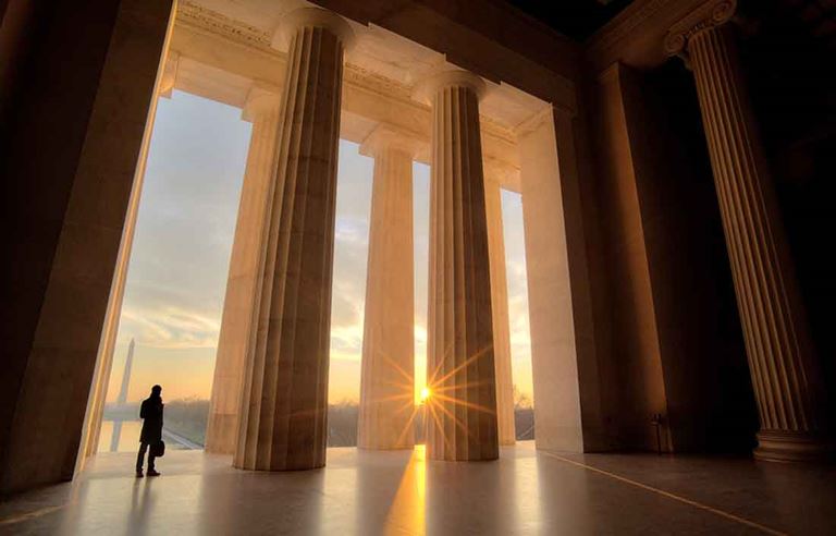 Photo of a person standing next to very large marble columns of a building.