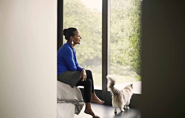 A woman sitting on the edge of her bed with a cat nearby.