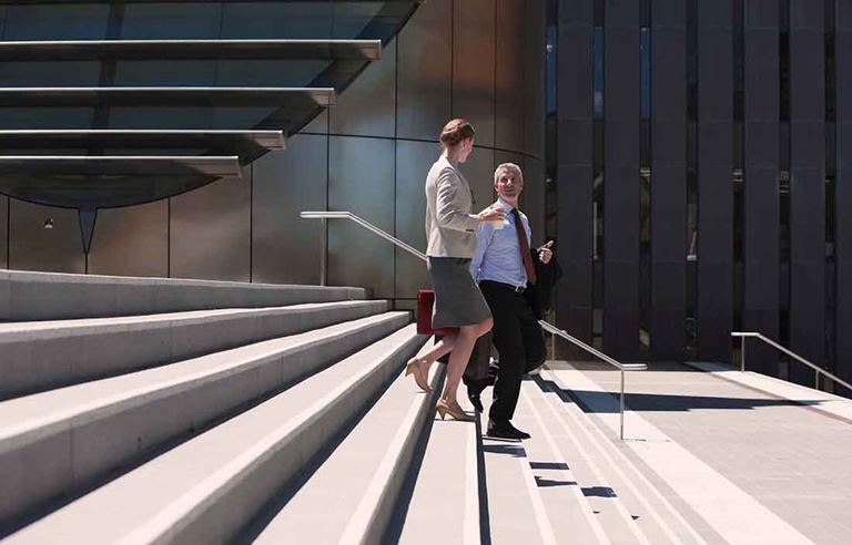 Two business professionals walking down a flight of stairs outside.