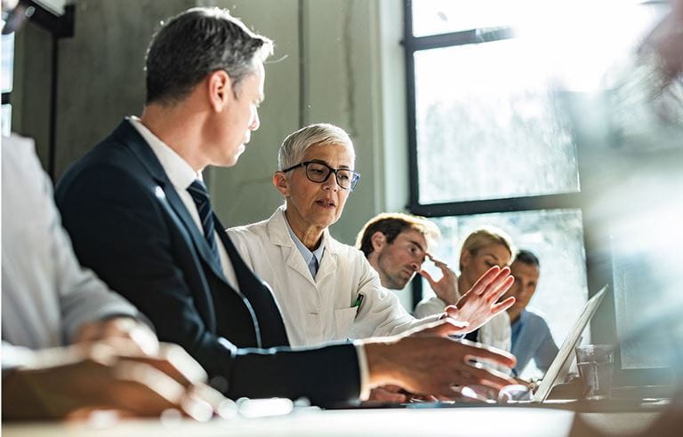 Business person sitting next to a doctor in a white doctor coat.