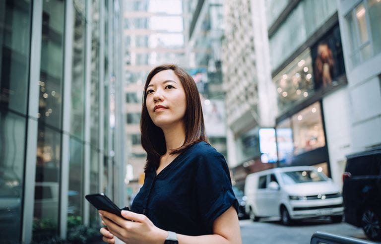 Person holding cell phone on a busy city street.