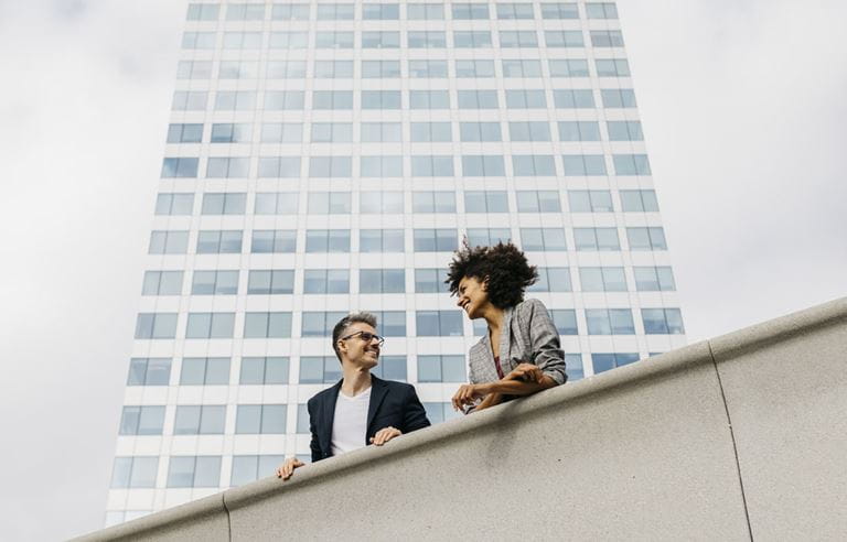 Two business professionals standing on the top of a building overlooking a city.